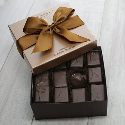 An open 24 piece assortment. Various chocolates from the assortment are pictured. The lid sits above the box and has a brown ribbon on it,