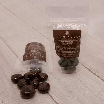 Two small, plastic bags of cherries sitting next to each other. One bag is laying down and has cherries spilled out.