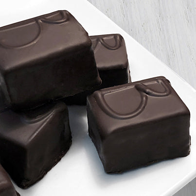 Multiple rectangle pieces of chocolates with the letter B on them sit on a white, square plate.