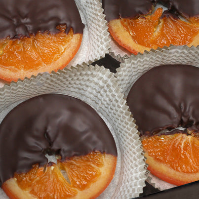 A close up of chocolate covered orange slices in white, paper cups.