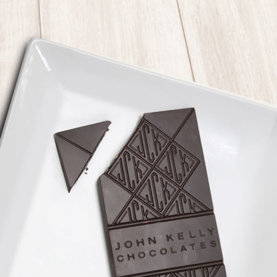 A dark solid bar with the top left corner cut off from it. The bar has a John Kelly Chocolates logo on it.
