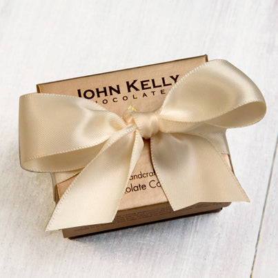 A small John Kelly Chocolates box with a large off-white bow on it.