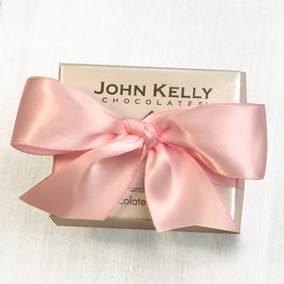 A small John Kelly Chocolates bow with a baby pink bow on it.