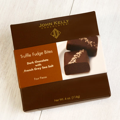 A dark brown box with a brown and white sleeve on it. The sleeve has an image of two grey salted truffle fudge bites on it.