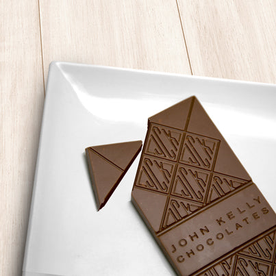 A milk chocolate solid bar with the top left corner cut off from it. The bar has a John Kelly Chocolates logo on it.