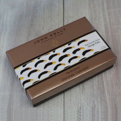 A closed box of the chocolate dipped orange peels. The box is brown with a white sleeve on it. The white sleeve has pictures of the chocolate dipped orange peels on it.