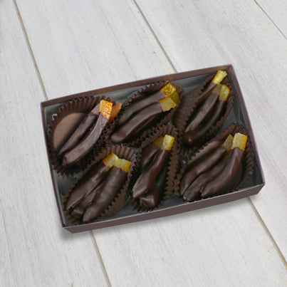 An open box shoes the chocolate dipped orange peels. There are six brown paper cups that each hold two of the chocolate dipped orange peels. Each peels is neatly put in the cup facing the same direction. The peels are not completely coated, leaving a little less than a fourth of the peel exposed.