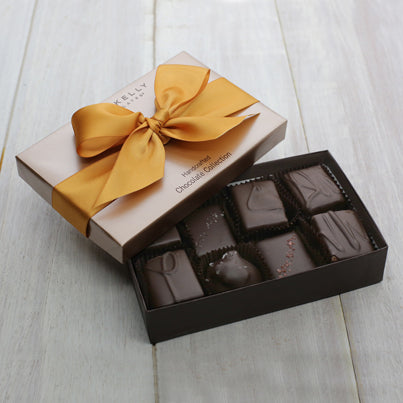 An open eight piece assortment. Chocolates from the assortment are present. The lid sits partially on the box and is tied with a gold ribbon.